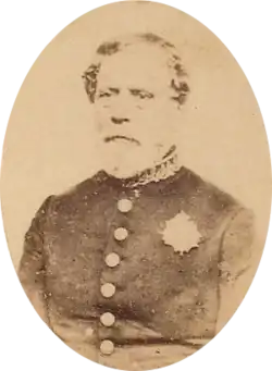 Sepia toned tintype photograph half-length portrait of an older, bearded man wearing a simple military frock coat with large buttons and a single medal over the left breast