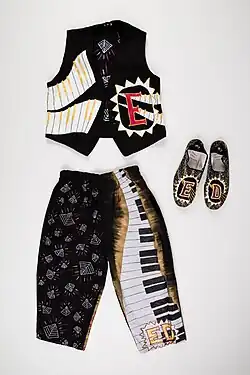 Laid flat on a white background is a waistcoat, trousers and shoes. All with decorative elements – stylized keyboards, patterns and a funky hand-drawn E with a triangle border on the waistcoat.
