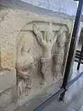 Crucifixion scene, sculpted in low relief on west end of base of chest tomb of Sir William de Tracy (d.1322), cleric, incumbent of Mortehoe; South transept.