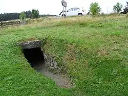 Narrow entrance to dark underground passage in a grassy field