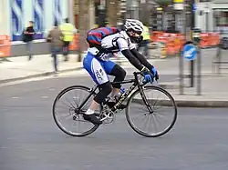 A man with sports clothes and a white helmet on a bicycle on a road.