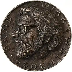Obverse of a bronze medal with the artistically designed portrait of David Wigg-Wolf in high relief. The sculpturally emphasized portrait is surrounded by a circular inscription with the name 'DAVID WIGG-WOLF' and the year '2024'.