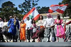 Lebanese flags flying in the background, while dancers in Lebanese traditional attire perform in the foreground
