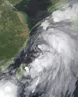 A photograph of a large and disorganized tropical storm off the east coast of China; the system's structure consists of multiple amorphous blobs of convection, with lower clouds making a circulation evident.