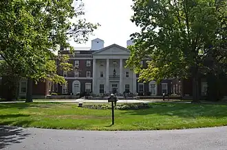 Four-story brick building surrounded by mature trees