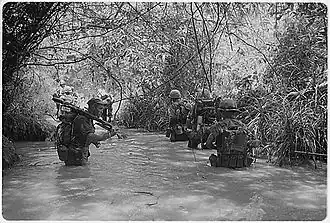 two columns of Marines wade through waist-deep water in a jungle