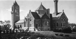 Engraving of a Romanesque building with a gabled roof, a square bell tower and a tall chimney