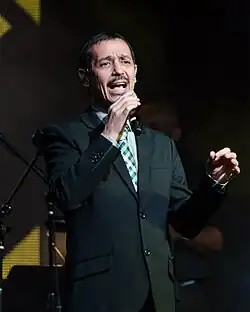 A man is facing the camera while holding a microphone with his right hand.