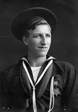 A young white man in a seaman uniform decorated with a star-shaped medal on the left breast, looking off into the distance.