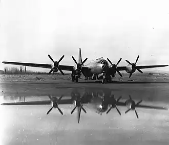 Black and white photo of a military aircraft powered by four propeller engines parked in an open area