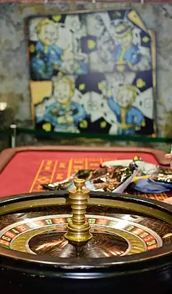 A close up photo of a roulette table. Behind the table is a poster featuring drawings of a character in a blue suit.