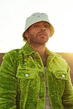 Feid wearing a fishing hat and a green wool jacket