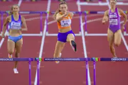 Photo of three athletes jumping over hurdles on a red athletics track