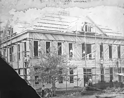 Photography of a two-story building under construction, prominently showing scaffolding and workers posing for the photograph