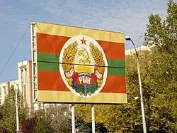 A road signboard with civil flag of Transnistria that superimposed with simplified version of the national emblem