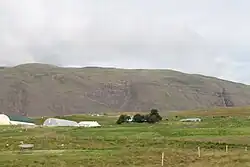 Farm buildings set into rolling green hills with a mountain looming behind