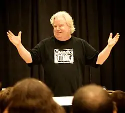 A man in giving a presentation to an audience in front of a theatrical curtain