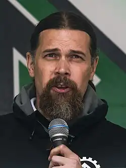 Vejdeland wearing a black hoodie and speaking into a microphone