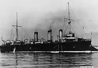 A large, black ship sits moored to a buoy; wispy smoke drifts up from its three smoke stacks.