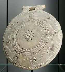 Roundish ceramic vessel (we can see the back) with decorations incised into it.