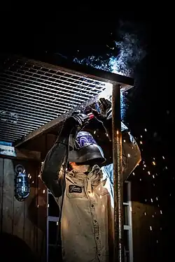 Welder stick welding a metal grate above their head