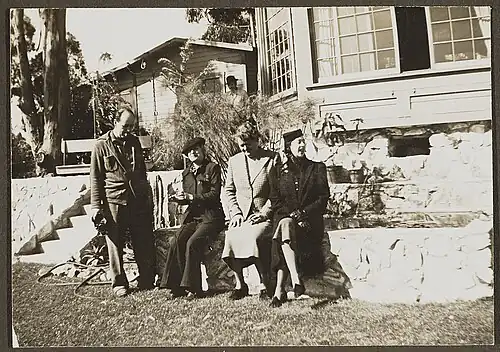 Gavin Arthur, standing, and Janet Flanner, Esther Murphy, and Solita Solano sitting on a rock wall, between 1945 and 1955