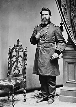 Photo of a dark-haired, bearded man with his right hand thrust into his coat like Napoleon. He wears a dark military uniform with two rows of buttons.