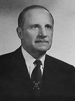 A middle-aged man in a suit, with receding hair and a neat moustache