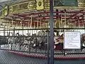A yellow and red historic carousel with a chain-link fence in the foregorund