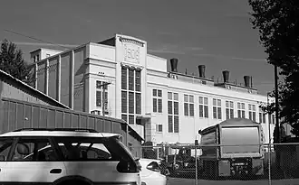 Photograph of the Seattle Electric Company Georgetown Steam Plant, from outside the compound in an industrial district. The peak of the large, dominating, white building shows the date 1906.