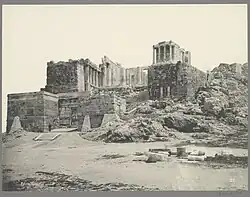 Black-and-white photograph of the gate, from a distance, showing the Temple of Athena Nike above