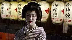 A geisha with lit paper lanterns behind her.