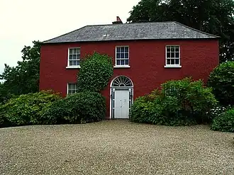Red two-story house amid trees and bushes