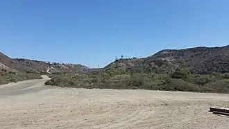 A valley, with schrub vegetation, a border barrier and highway in the distance