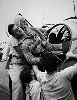 Crewmen aboard USS Saratoga lift a wounded aviator out of a Grumman TBF Avenger's rear turret. Photo by Lt Wayne Miller.