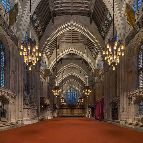 A large medieval hall with pointed arches and a red carpet