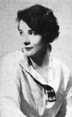 A young white woman with dark hair, wearing a light-colored blouse with an open collar
