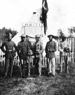 A group of five soldiers in front of a tent with a sign labeled Haiti
