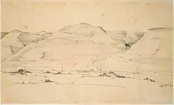 Several hills dominate the mostly barren landscape in the foreground. A road moves from the foreground into a pass formed between the hills.