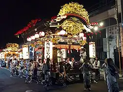 A festival float cart with taiko drummers lit up at night