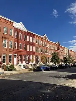 The photo shows three story red brick houses along a sunny, tree-lined streetl.