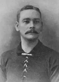 Head and upper torso of a white man with a moustache wearing a dark sports shirt.