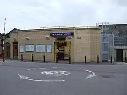 A beige-bricked building with a rectangular, blue sign reading "HIGH BARNET STATION" in white letters all under a blue sky with white clouds