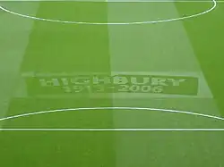 A photograph of a green football turf, with the words Highbury, 1913–2006 etched in the middle.