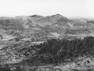 A series of ridgelines and steep hills in the distance, with Maryang-san on the right. In the foreground is a heavily vegetated knoll, with a valley in the intervening ground.