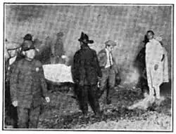 Black and white photo of firemen carrying a stretcher with a body covered in a white sheet