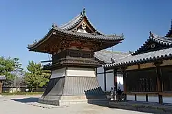 Small wooden tower shaped structure with a flared lower part and a hip-and-gable roof.