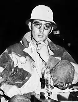 Portrait photograph of a 33-year-old man wearing a denim jacket, a bucket hat, and sunglasses