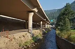 View underheath an elevated highway on the shores of a narrow river flanked by rocks and walls