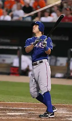 A man in a blue baseball uniform with a blue helmet watches the ball fly after swinging his black bat.